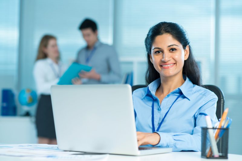 Closeup portrait of a young business lady typing and looking at camera on the foreground